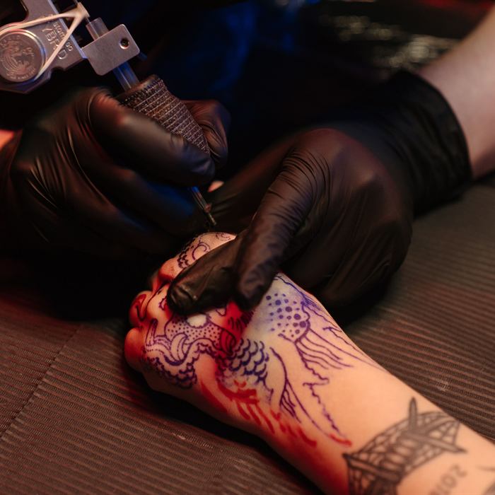 Close-up of a hand tattoo being outlined under coloured light